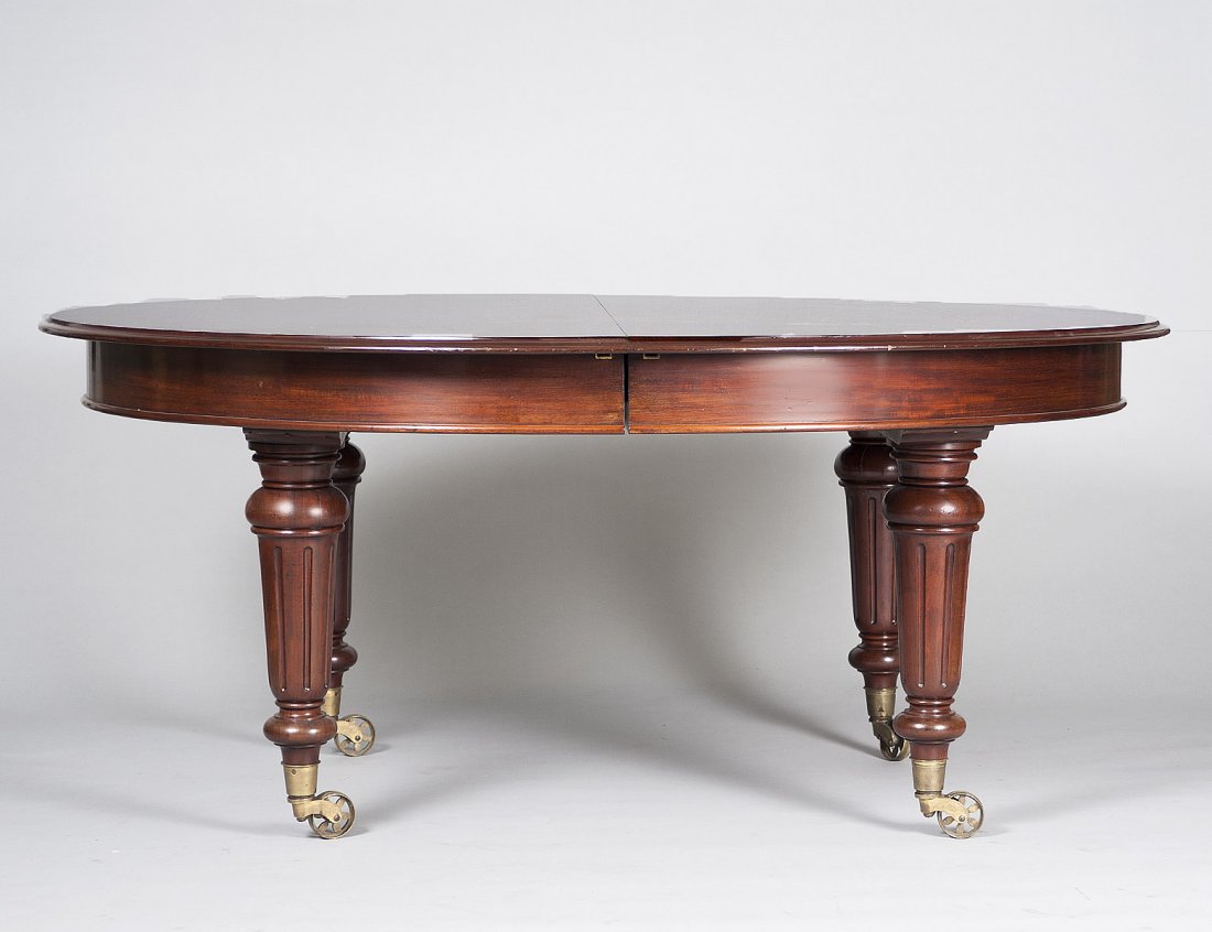 WILLIAM IV STYLE MAHOGANY DINING TABLE: The oval top raised on circular tapering reeded legs ending in brass casters. Height 29 ¾”. Width 67”. Depth 56 ¼”. (1000/1500)