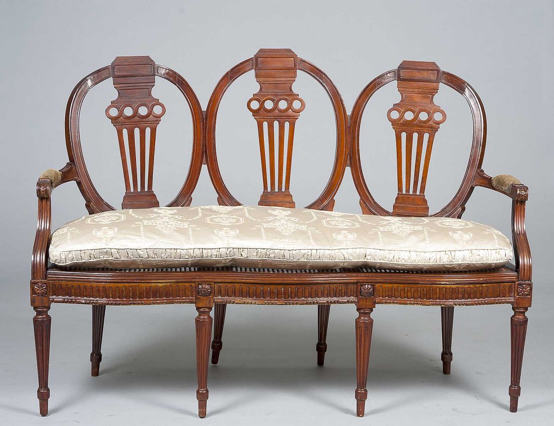 GEORGE III STYLE MAHOGANY TRIPLE BACK SETTEE: Each oval backrest with pierced splat above the cane seat with loose cushion, raised on circular reeded tapered legs. Length 56 ½”. (500/700)