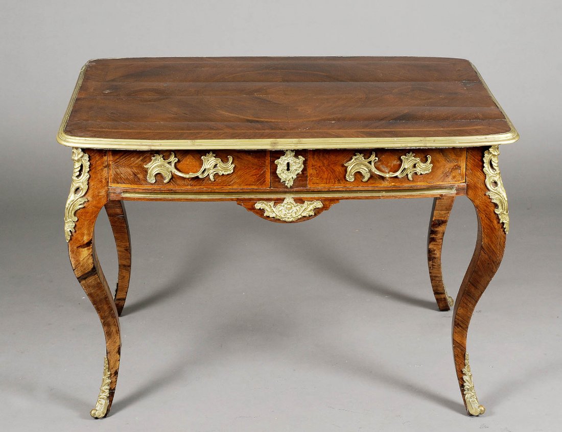 LOUIS XV STYLE MAHOGANY BUREAU PLAT: French. 19th Century. The quarter veneered rectangular top inlaid with geometric motif and with gilt bronze edge above two frieze drawers, raised on cabriole legs mounted with gilt bronze chutes and s