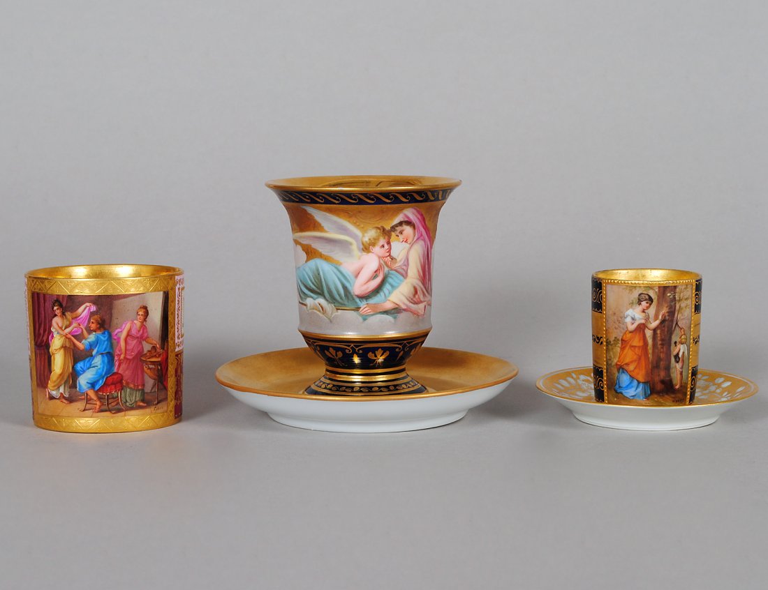 GROUP OF THREE VIENNA PORCELAIN CUPS AND SAUCERS: Austrian. Circa 1900. Comprising: cup painted with "Apelles Malt die Venus", demitasse cup and saucer and a hot chocolate cup and saucer "Amor Psyche". (400/500)