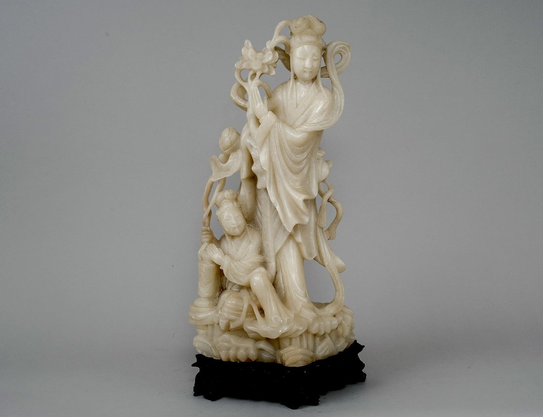 LARGE CARVED SOAPSTONE GROUP: Chinese. Depicting Guanyin with an attendant. Height 19 7/8”. On a carved wood stand. (600/800)