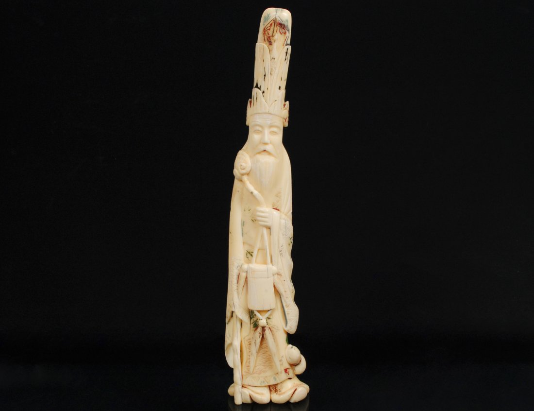 CARVED IVORY FIGURE OF AN IMMORTAL: Chinese. With tall cap, holding a scepter and a container. Height 9 3/4". (350/450)