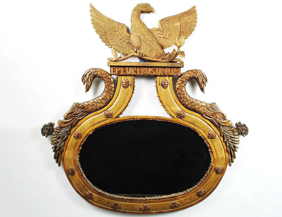 EMPIRE STYLE CARVED AND GILTWOOD MIRROR: 20th Century. With an eagle crown above the oval mirror with stylized dolphins. Measuring 43 1/2" by 42 3/4". (600/800)