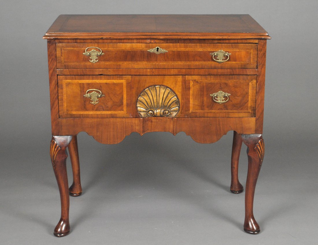 QUEEN ANNE STYLE WALNUT LOW BOY: The half veneered and cross banded molded top above two long drawers, the lower part carved with a shell, raised on cabriole legs ending in pad feet. Height 29 1/4". Width 30". Depth 17 3/4". (600/800