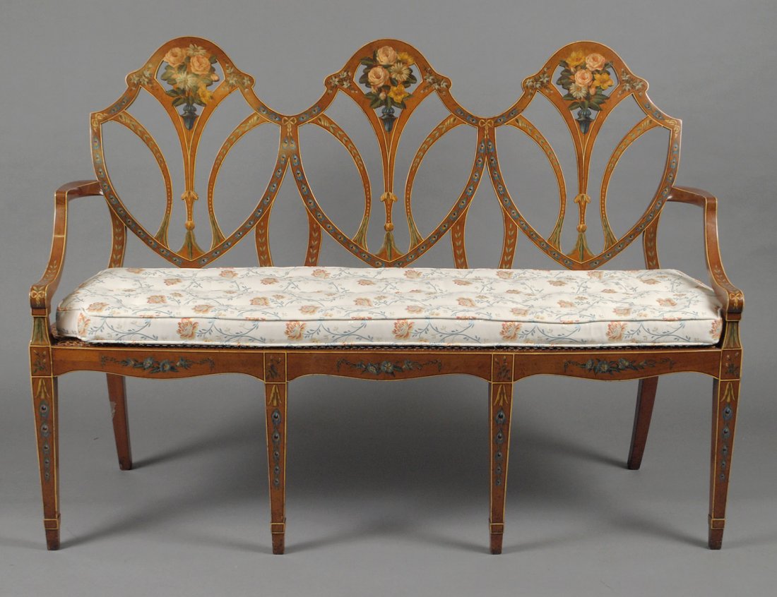 ADAMS STYLE PAINTED SATINWOOD TRIPLE BACK SETTEE: Each shield shaped backrest painted with flowers, flanked by short armrests above the cane seat with loose cushion, raised on square tapered legs. Length 57". (500/700)