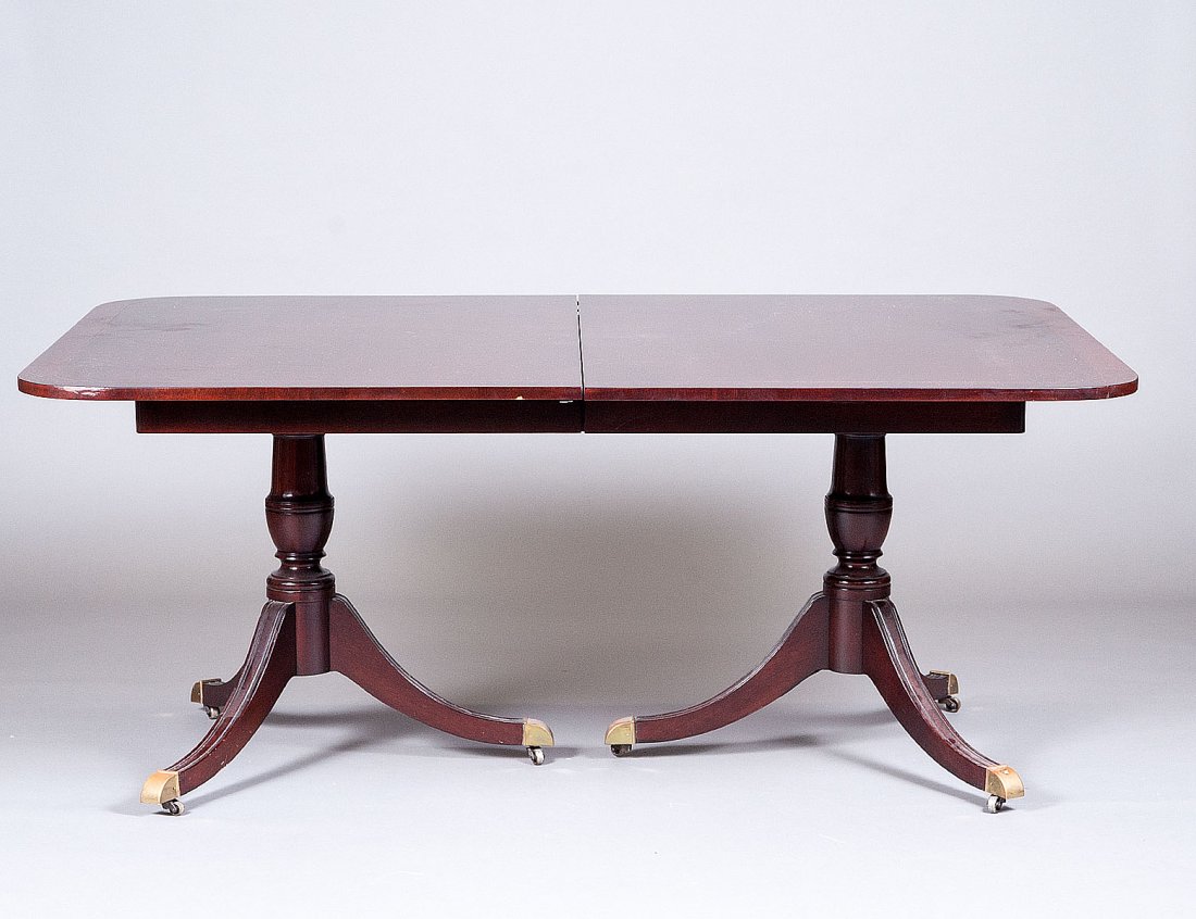 GEORGIAN STYLE TWO PEDESTAL MAHOGANY DINING TABLE: American. The cross banded top above the baluster standards raised on reeded downswept legs ending in brass caps and casters. Height 29". Width 69 1/4". Depth 46". With four extension leaves each meas