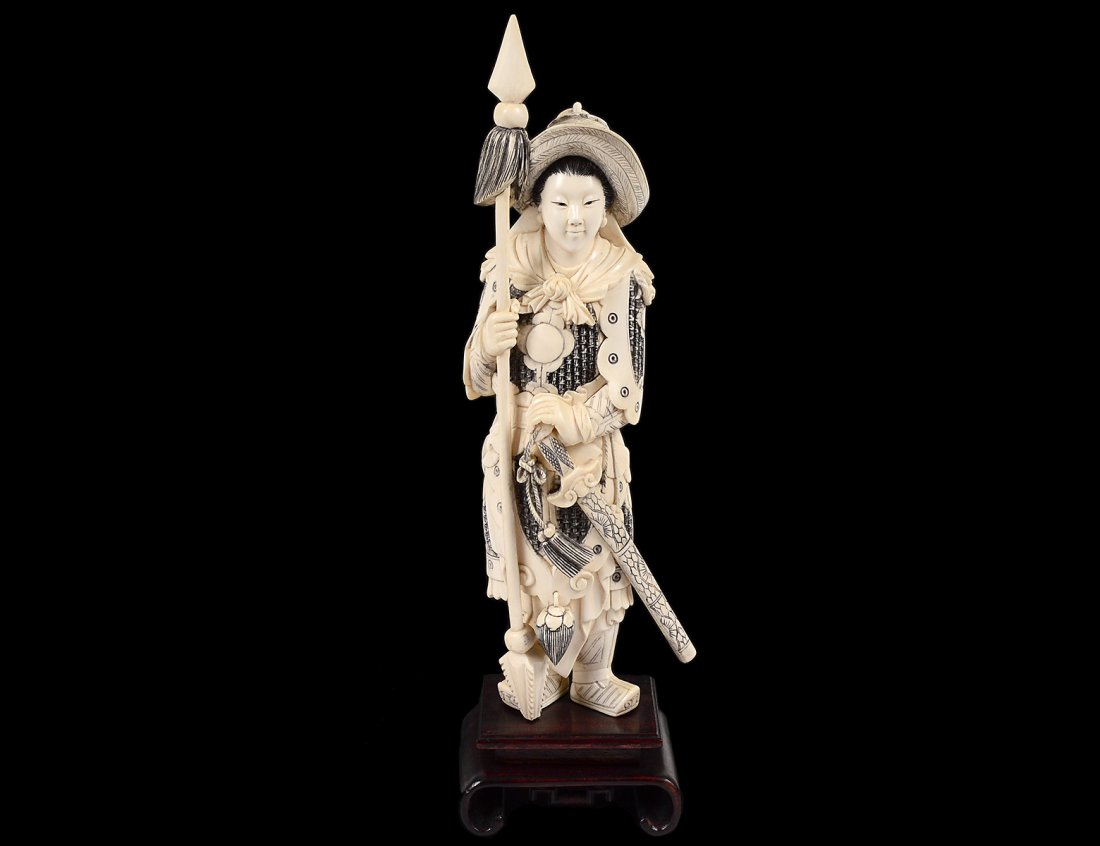 CARVED IVORY FIGURE OF A FEMALE WARRIOR: Chinese. Dressed in armor and straw hat holding a lance. Height 11 3/4". Mounted on a wood stand. (700/900)