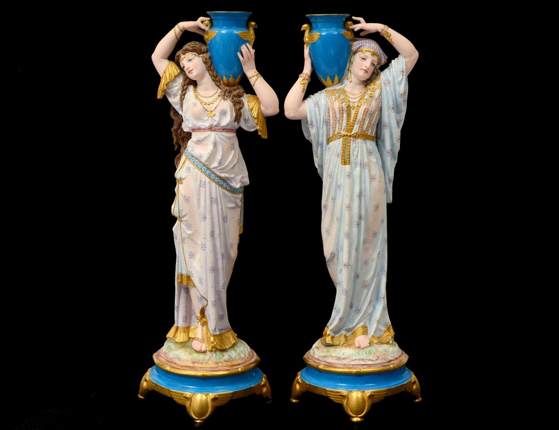 GOOD PAIR OF BISQUE AND PORCELAIN FEMALE WATER CARRIERS: French. Paris. 19th Century. Each in a long robe carrying an amphora on the shoulder. Height 19 1/4". (1000/1500)