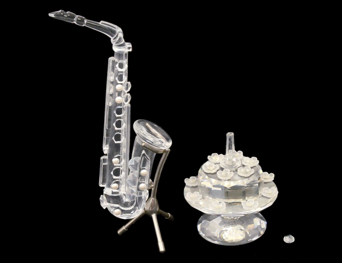 TWO SWAROVSKI CRYSTAL ARTICLES: Comprising: saxophone with metal stand and a birthday cake. Each in original box. (75/100)
