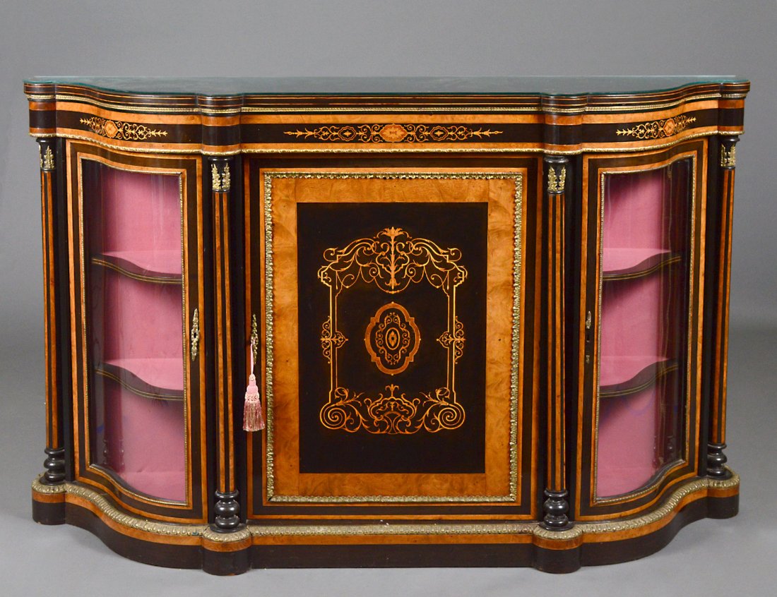 NAPOLEON III INLAID SATINWOOD AND EBONIZED CREDENZA: Circa 1865. The shaped top above a central inlaid door and a pair of glazed doors interrupted by tapering columns, raised on a conforming plinth, the whole mounted with gilt bronze appointments. Heigh