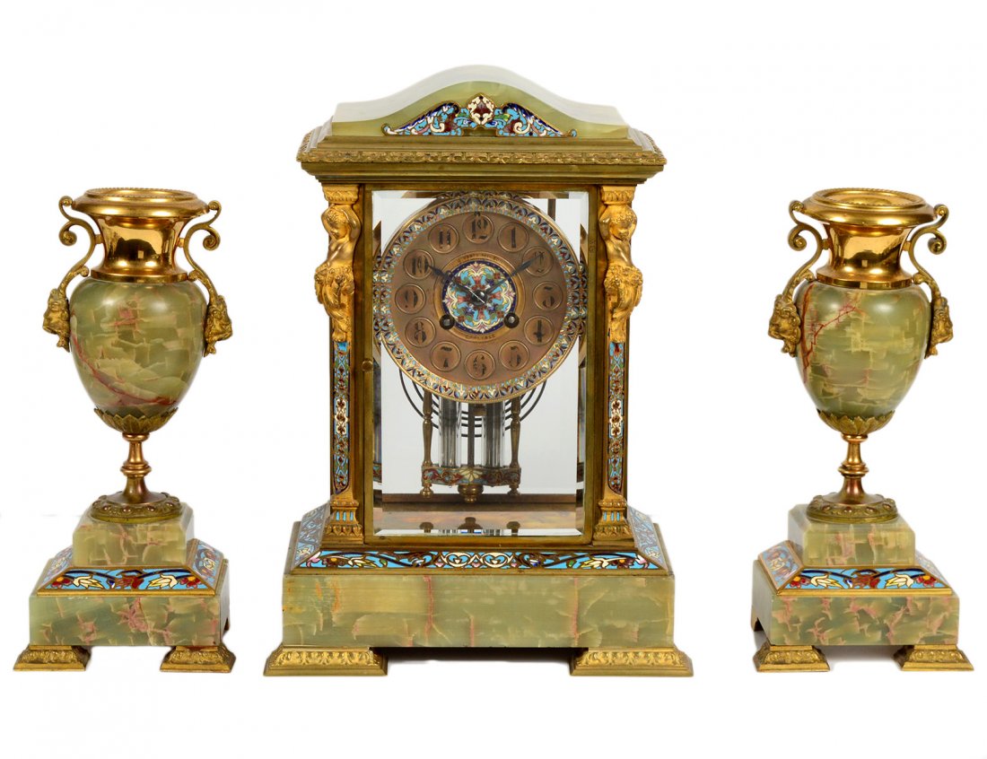 THREE PIECE GILT BRONZE, CHAMPLEVE ENAMEL AND ONYX: French. Circa 1910. Movement stamped Medaille D'Argent. The dial signed J. Varty Wilson, Carlisle. Of architectural form. Accompanied by a pair of urns. Height of clock 13 1/8". (3000/4000)
