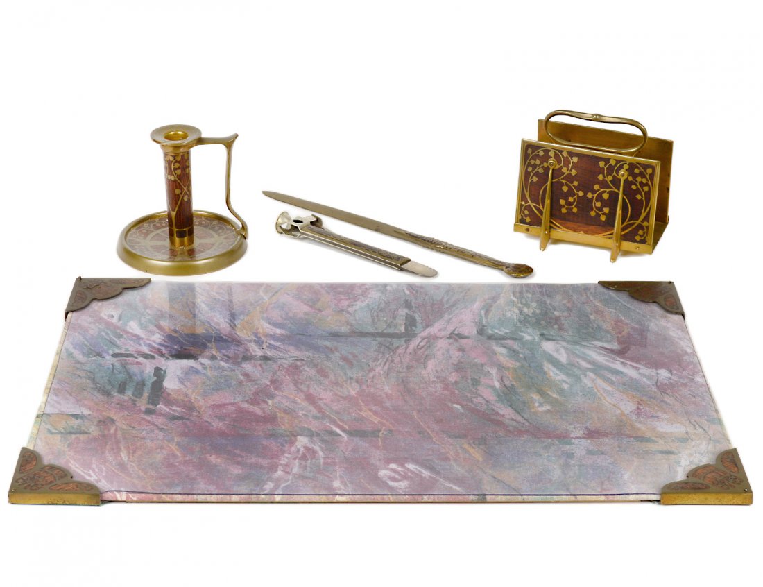 FIVE PIECE ARTS & CRAFTS DESK SET: German. Circa 1920. Comprising: letter rack, chamber stick, letter opener, cigar cutter and four blotter ends. Each inlaid with brass. (350/450)
