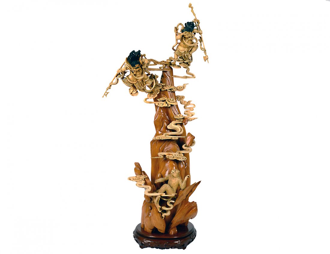 OUTSTANDING CARVED IVORY AND WOOD GROUP: Chinese. 19th Century. Carved as a precipitous mountain surrounded by clouds with two celestial warriors watching a monkey. Height 28 1/4". On a carved wood stand. (Cond: minor losses and restorations