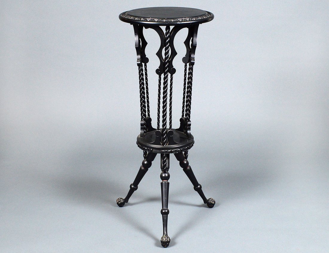 AESTHETIC MOVEMENT CARVED AND EBONIZED WOOD PEDESTAL: American. Circa 1875. With circular top above spiral supports, raised on turned legs joined by a platform stretcher, ending in claw and ball feet. Height 34". Diameter 14 1/4". (100/500)