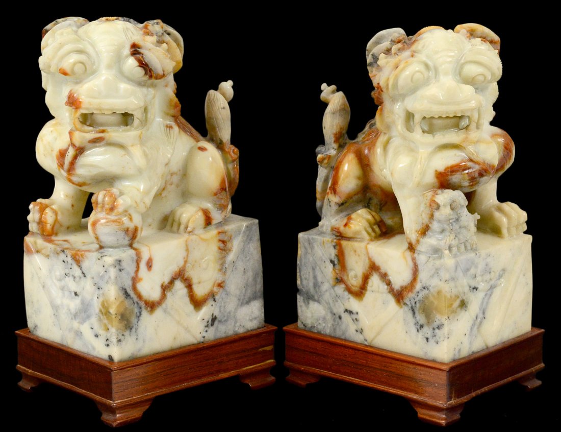 PAIR OF CARVED SOAPSTONE FU DOGS: Oriental. Each seated on a plinth. Height 6 1/8". With wood stands. (200/300)