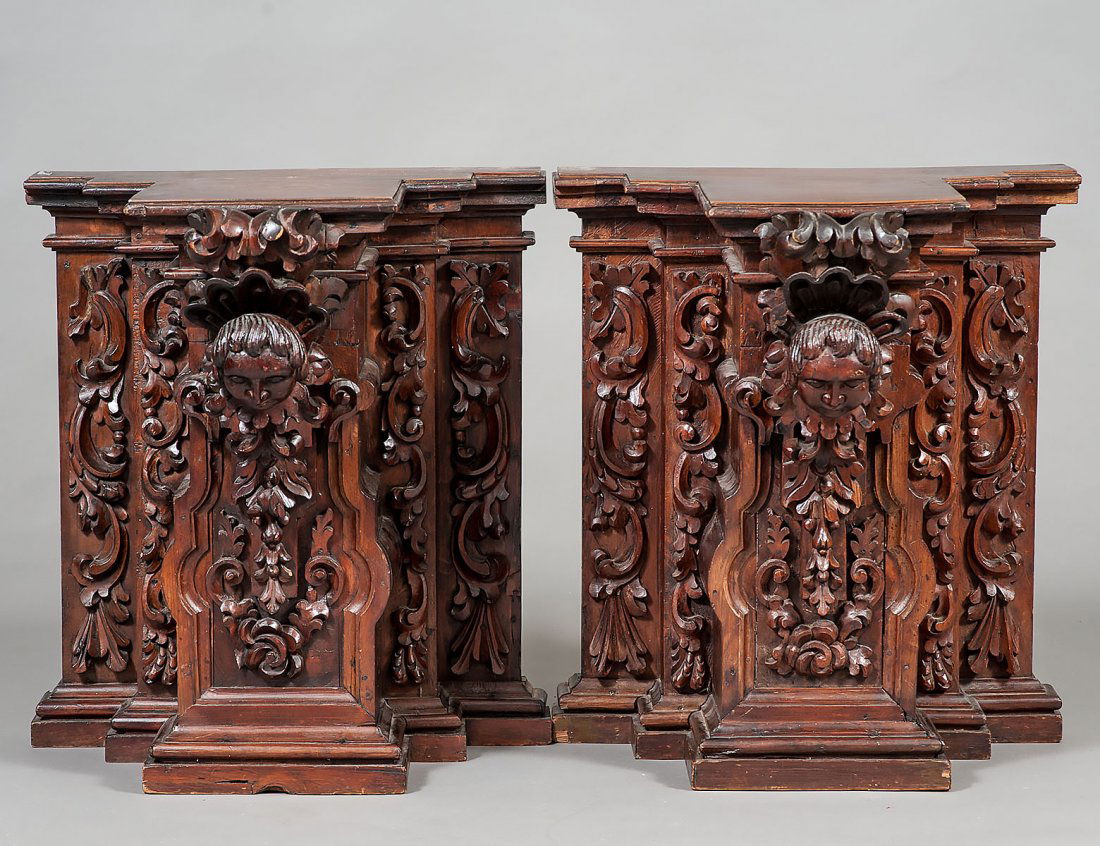 PAIR OF CARVED WALNUT AND MAHOGANY PEDESTALS: European. Late 19th Century. Each with stepped top above an angel head and foliate panel, raised on a conforming base. Height 24â€. Width 22 5/8â€. Depth 20â€. (700/900)