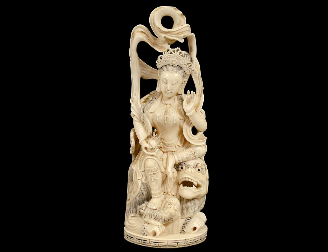 FINELY CARVED AND PARCEL GILT IVORY DEITY: Indian. 20th Century. Seated on a fu dog with a cub holding the flaming pearl. Height 10". On a wood stand. (1000/1500)