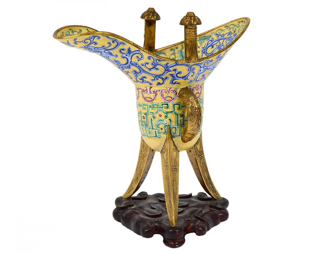 PEKING ENAMEL ARCHAIC FORM WINE VESSEL: Chinese. On brass supports, with blue decoration on a yellow ground. Height 7". On a carved wood stand. (250/350) Note: This lot is being re-offered for sale due to the fact that Huahin Sama of Japan