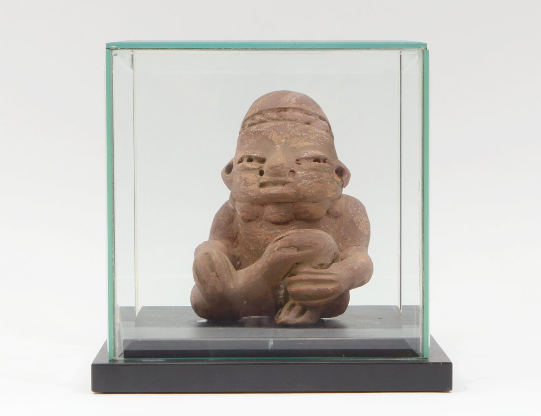 PRE-COLOMBIAN JALISCO NAYARIT SEATED POTTERY......: TOMB FIGURE Height 6 3/4". Mounted on a wood base with glass casing. (300/400)