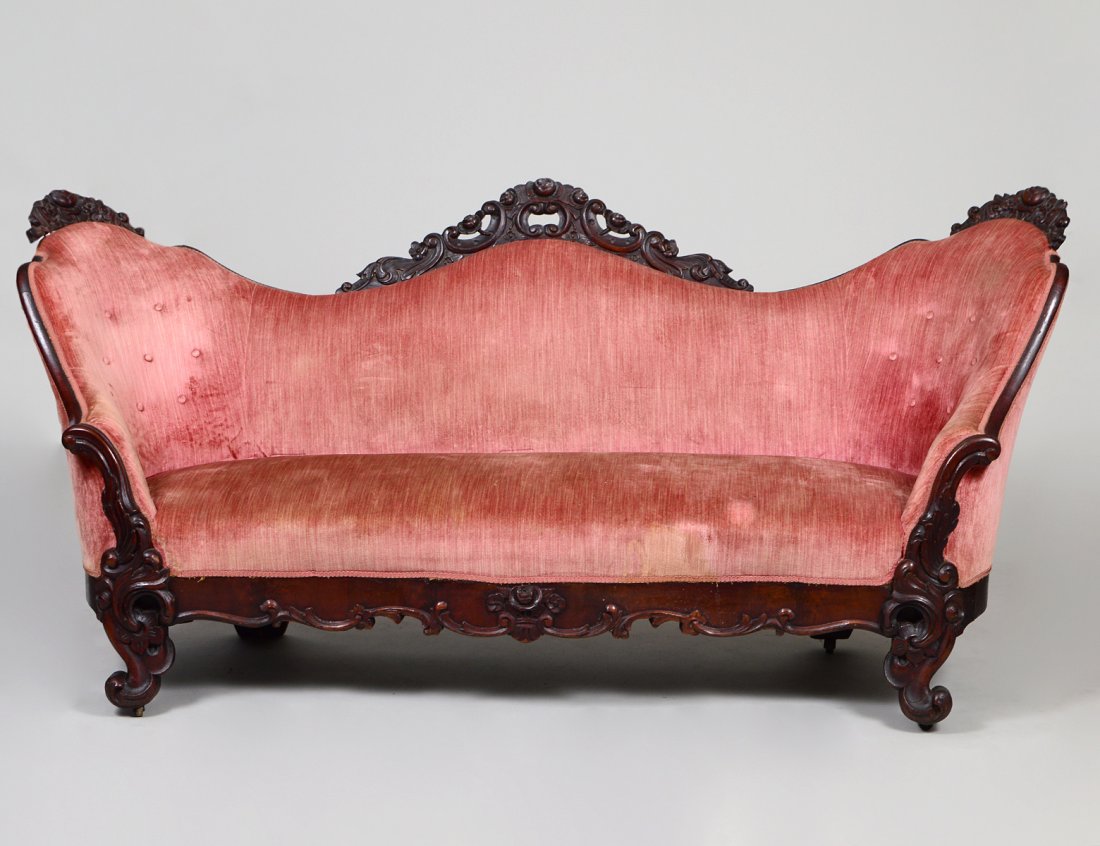 VICTORIAN ROCOCO REVIVAL CARVED WALNUT SETTEE: Circa 1860. The triple-arched upholstered back carved with foliage and scroll, the seat skirt and scrolled legs similarly carved. Length 7’ 5”. Height of back to floor 40½”. (Cond: minor repair