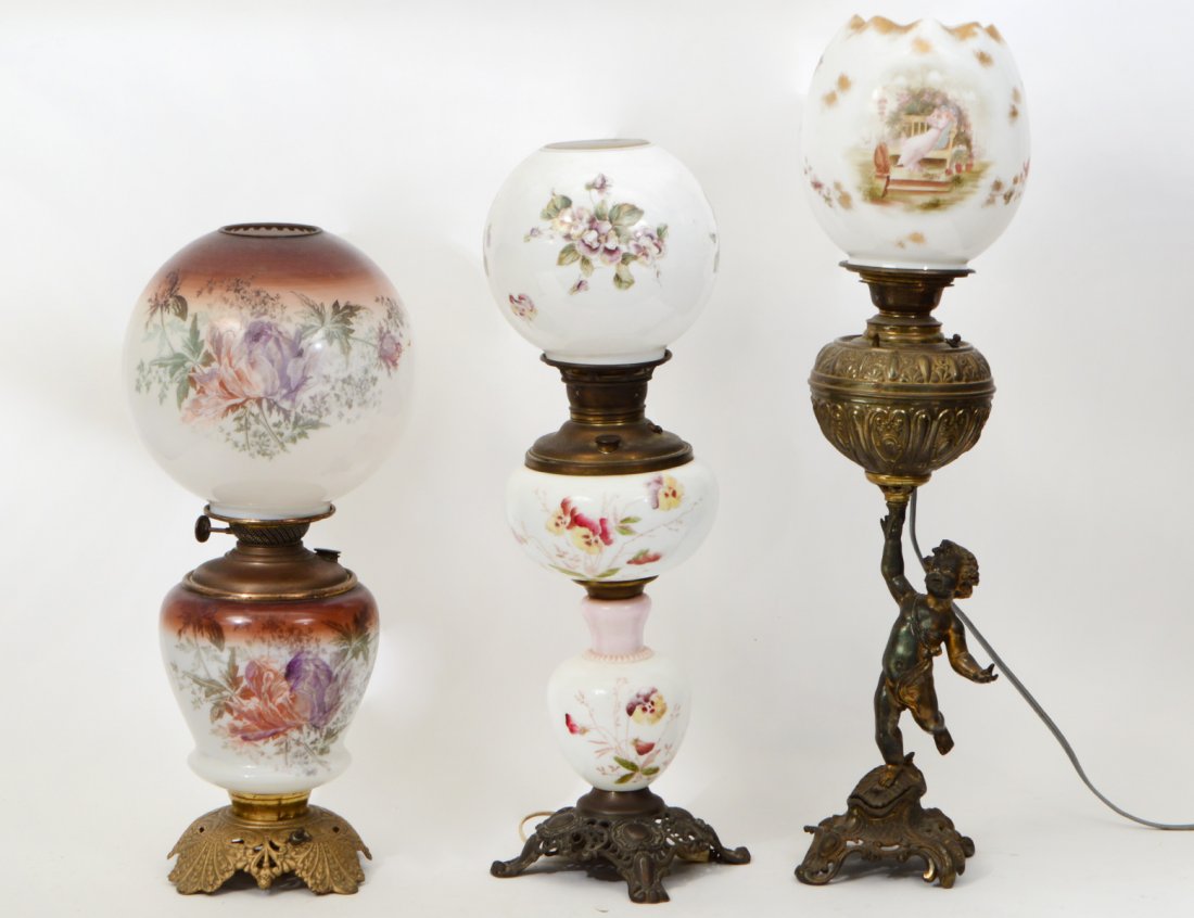 GROUP OF THREE "GONE WITH THE WIND" OIL LAMPS: Two with floral painted decorations; one with a gilt metal cherub base. With matching globes. Now electrified. (Cond: some chips and nicks) (300/400)