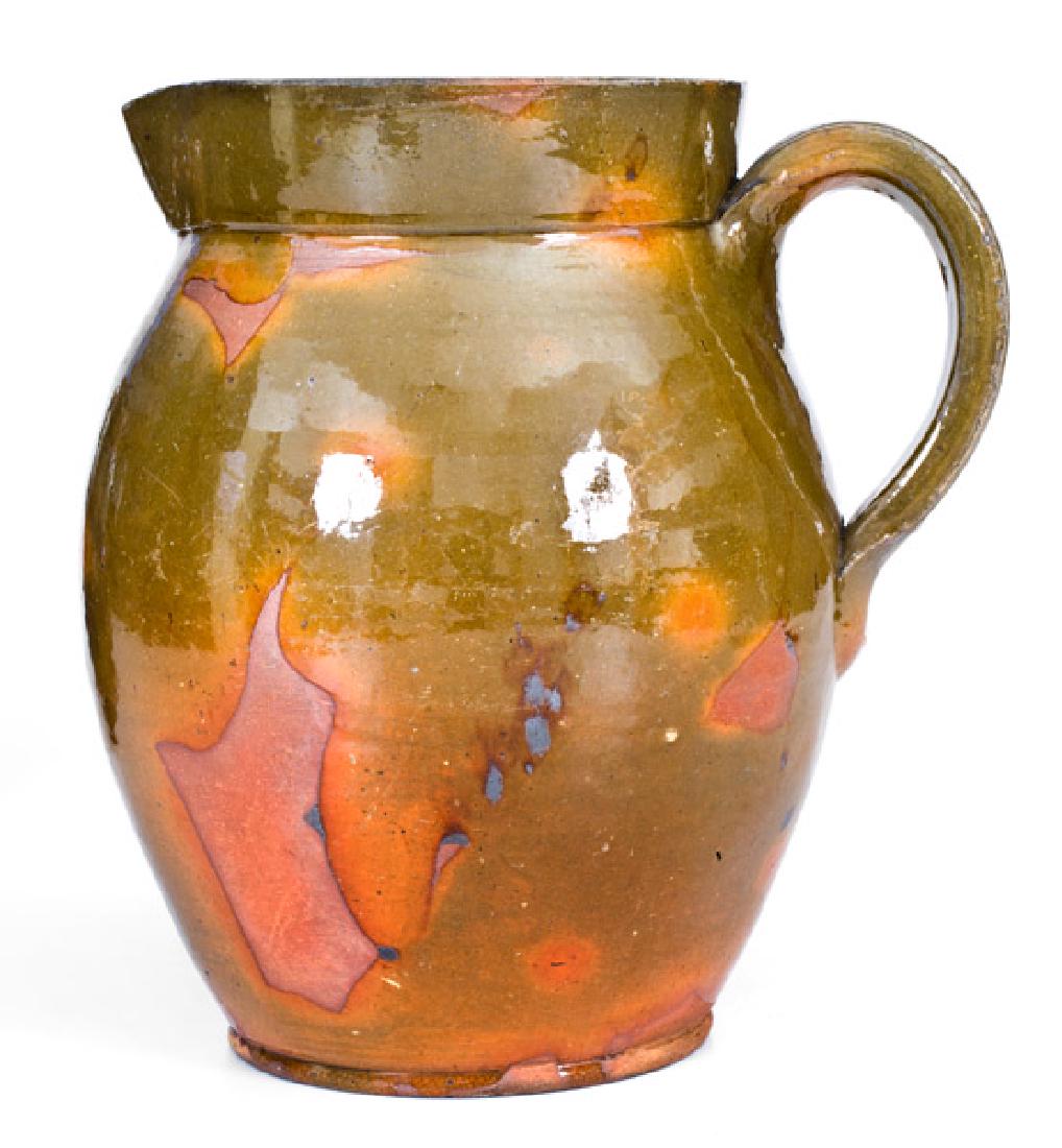 New England Redware Pitcher: Glazed Redware Pitcher, New England origin, circa 1840, ovoid pitcher with footed base, ribbed handle, and short, flaring collar, the surface decorated with light manganese accents and covered in a cl