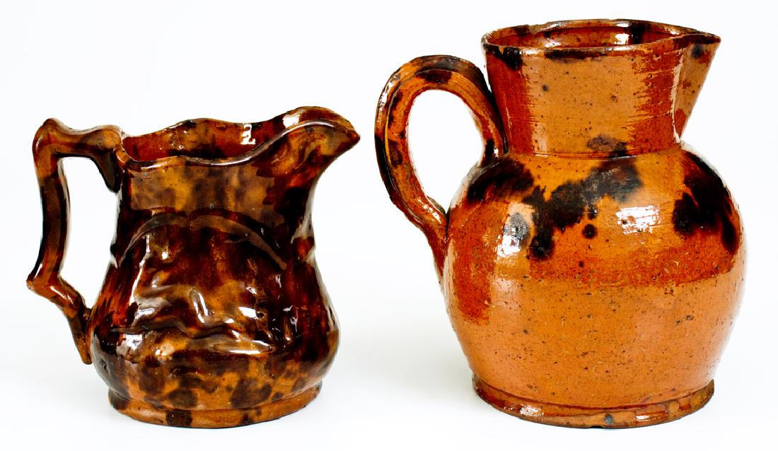 Lot of Two: Pennsylvania Redware Pitchers incl. Unusual: Two Glazed Redware Pitchers, PA origin, 19th century, a molded pitcher with relief leaping deer and hanging game bird motifs, decorated with splashed manganese and covered in a clear lead glaze; paire
