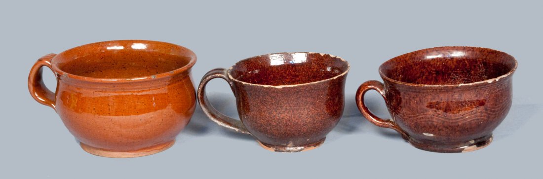 Lot of Three: Glazed Redware Mush Cups: Three Glazed Redware Mush Cups, American, early to mid 19th century, two early, thin-walled mush cups with lead-and-manganese-glazed surfaces, one of which includes wavy combed incising; together with