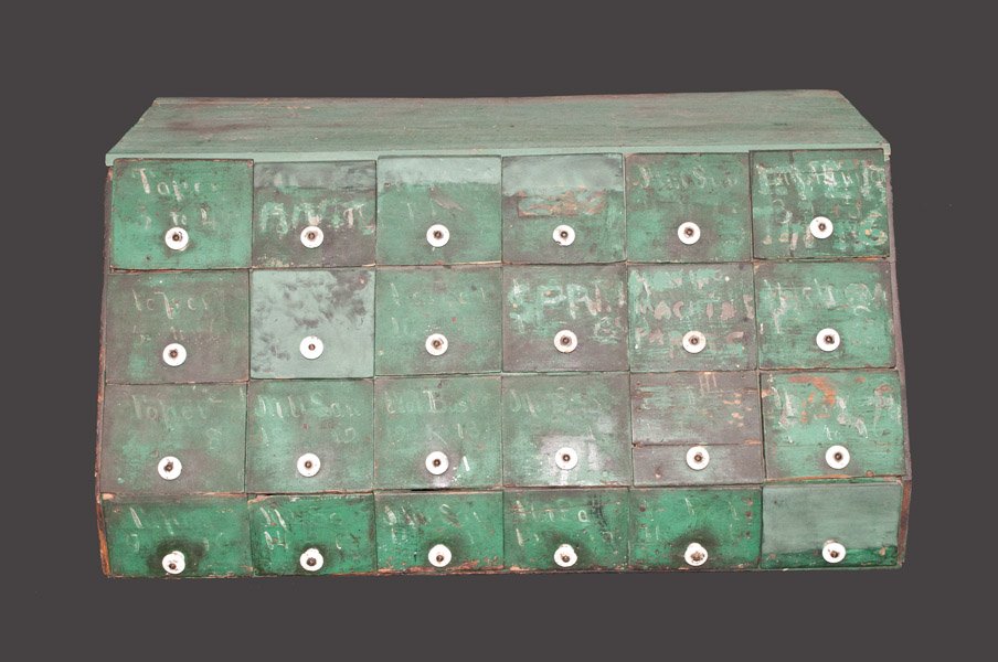 24 Drawer Apothecary Cupboard in Green Paint: Twenty-Four Drawer Apothecary Cupboard in Green Paint, American, late 19th century, slant-front apothecary cupboard with unusual row of smaller drawers at base. Drawers with porcelain knobs and traces