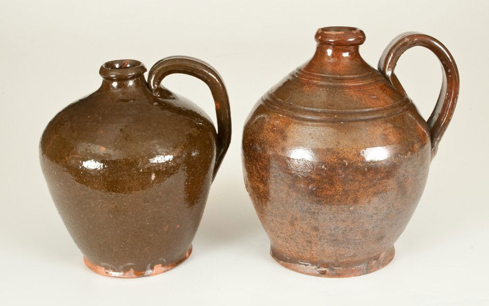 Lot of Two: Ovoid Redware Jugs: Two Glazed Redware Jugs, American, 19th century, one with tooled shoulder, footed base, and lead-glazed surface over a mottled green and orange, the underside with the later carved inscription, "M F F