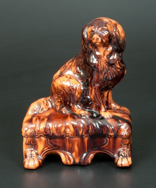 Unusual Redware Molded Redware Dog on Footstool Figure: Unusual Glazed Redware Spaniel on Base, fourth quarter 19th century, molded, detailed figure of a spaniel. seated on a footstool base with tassels and paw feet. Surface decorated with streaks of manga