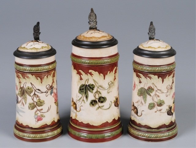 Three Mettlach Steins: .5L, 966(2184), PUG, inlaid lid (with browning), gnomes drinking, by Schlitt; two .3L, 966(2184), PUG, inlaid lid, gnomes drinking, signed Schlitt Provenance: Dennis Galloway Estate, Etowah, NC