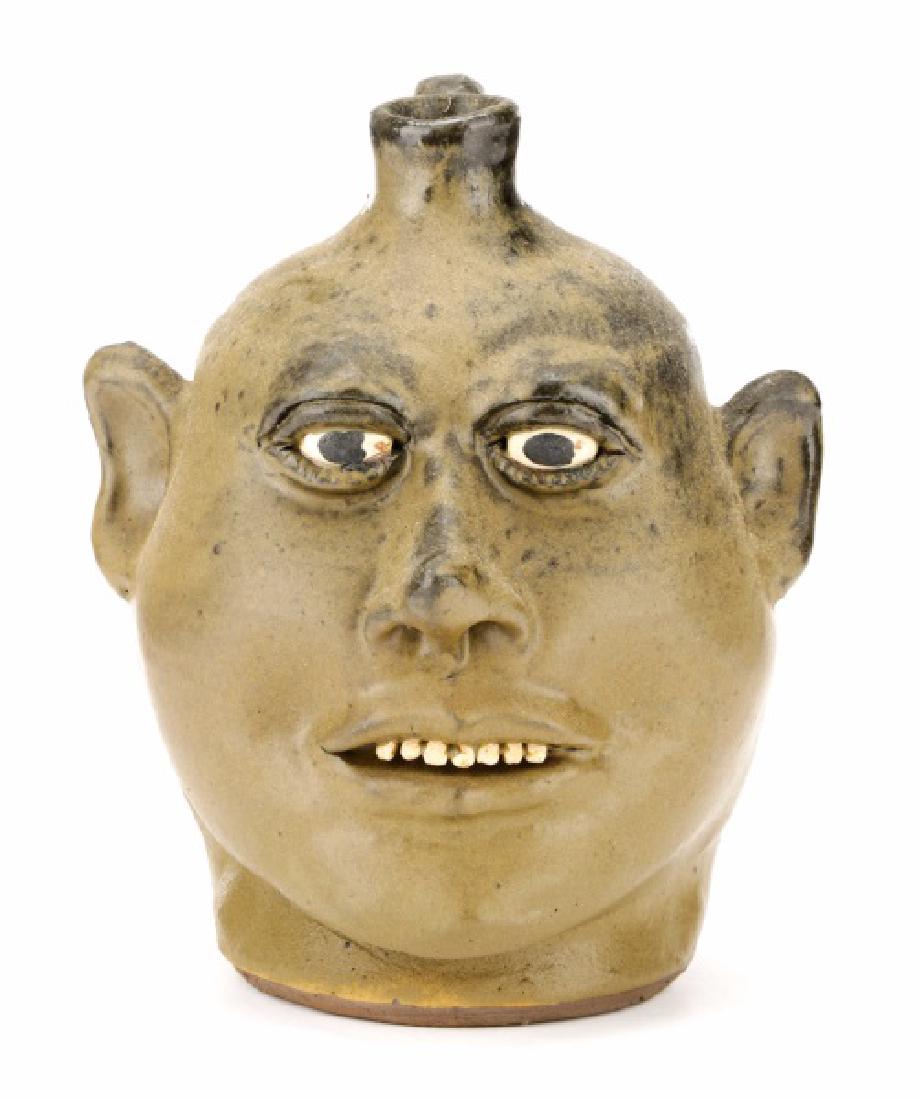 Signed Lanier Meaders Face Jug with Seven Teeth: Lanier Meaders (American, Georgia, 1917-1998), circa 1970s. A dark to light green underfired glazed face jug, having painted white eyes and black pupils, incised eyelashes, a pointed nose and ears, se