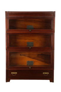 Globe Wernicke Mission Elastic Bookcase Unit: Globe Wernicke Company (American (Ohio) 1893-1987), first quarter 20th century. A Mission pattern barrister or 'elastic' bookcase having three sections with glass lift doors, over a single base drawer