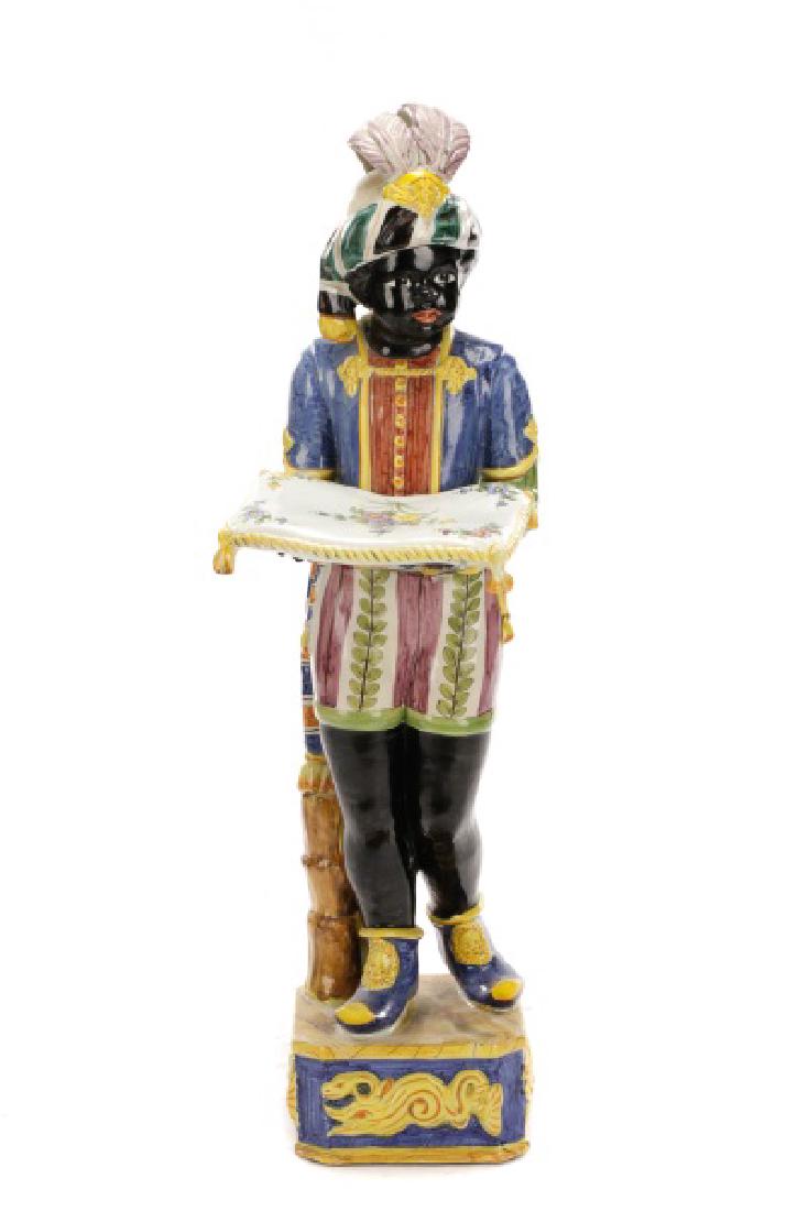 Majolica Blackamoor Figurine with Pillow: Italian, late 19th/20th century. A large majolica glazed pottery Blackamoor figure, wearing a plumed turban and a blue, red, and gold coat over purple striped shorts with green foliated patterning, on
