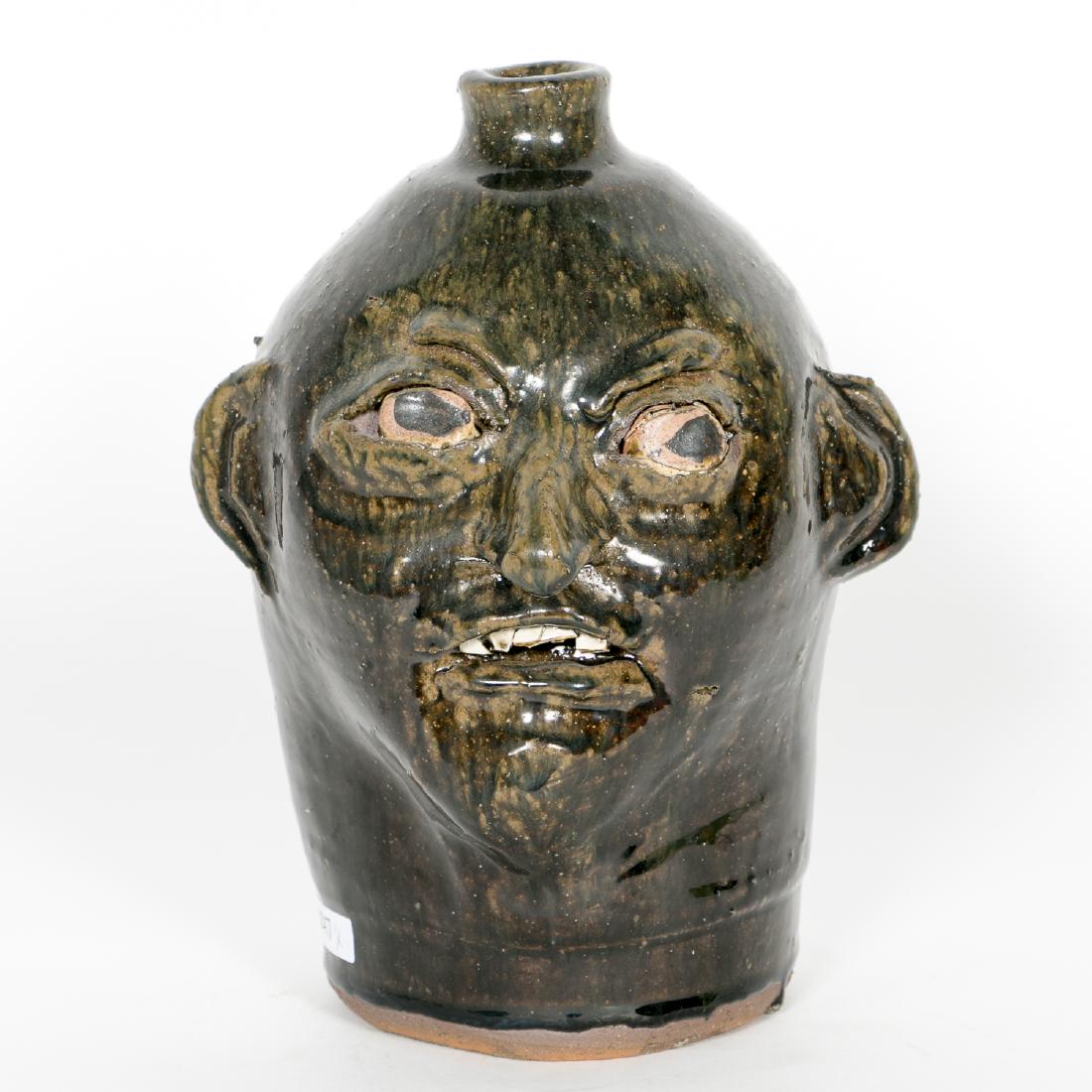 Chester Hewell, Face Pottery Jug with Teeth: Chester Hewell (American, b. 1950 - ) A face jug with green alkaline glaze and teeth Signed on underside Approx. h. 10.75" Provenance: From the Lifetime Collection of Dick and Betty Hoepfinger, of Mar