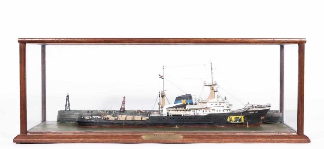 Cased Model Ship, "Zwarte Zee" Circa 1964: Robert Mouat (British, 20th Century). A 1/8" scale model of the Zwarte Zee rescue tug boat hand painted and assembled in a docked position; presented in a large wooden display case. Marked with a plaq