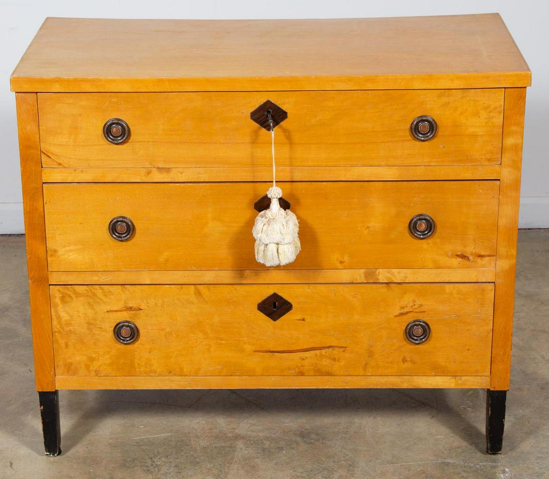 20th Century, Biedermeier Three Drawer Chest: Continental, early 20th century. A three drawer birch commode with single plank top, each drawer has central diamond shaped key holes flanked with floral pattern ring pulls and terminating to four bla