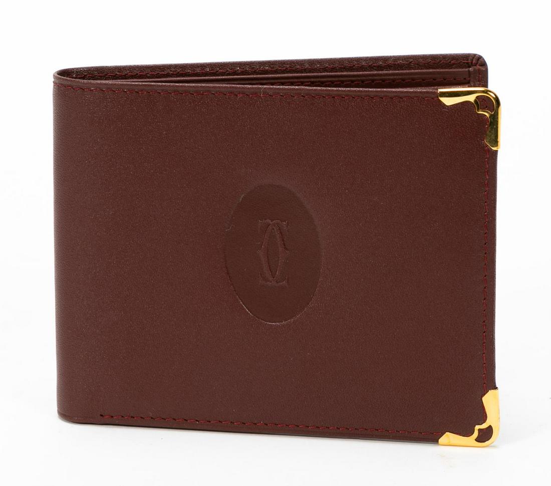 Cartier Burgundy Six Card Bifold Wallet: Cartier (French, est. 1847), 21st century. A "Must de Cartier" burgundy six card bifold wallet with gold tone metal corners and the double "C" embossed logo. Marked on interior and including card with