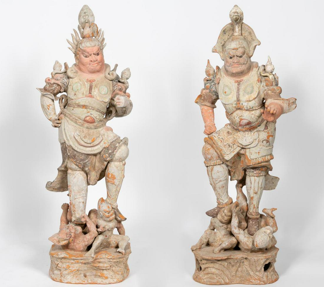 Two Chinese Tang Dynasty Earthenware Lokapala: Chinese, Tang Dynasty. Two painted earthenware Lokapala with helmets and armored bodies with flame form finials emanating from dragon form epaulettes on the shoulders. The figures standing on imps, on