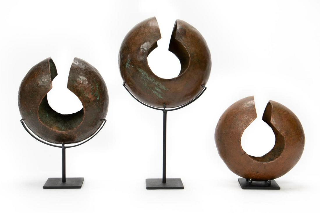 3 Mbole Tribe Copper Currency Anklets w/ Stands: African, 20th century. A group of three DRC Mbole copper currency anklets on custom made stands. Approx. h. 9.75" (tallest), h. 18.25" (tallest on stand). w. 8.5" (copper piece), h. 9.25" (shortest on