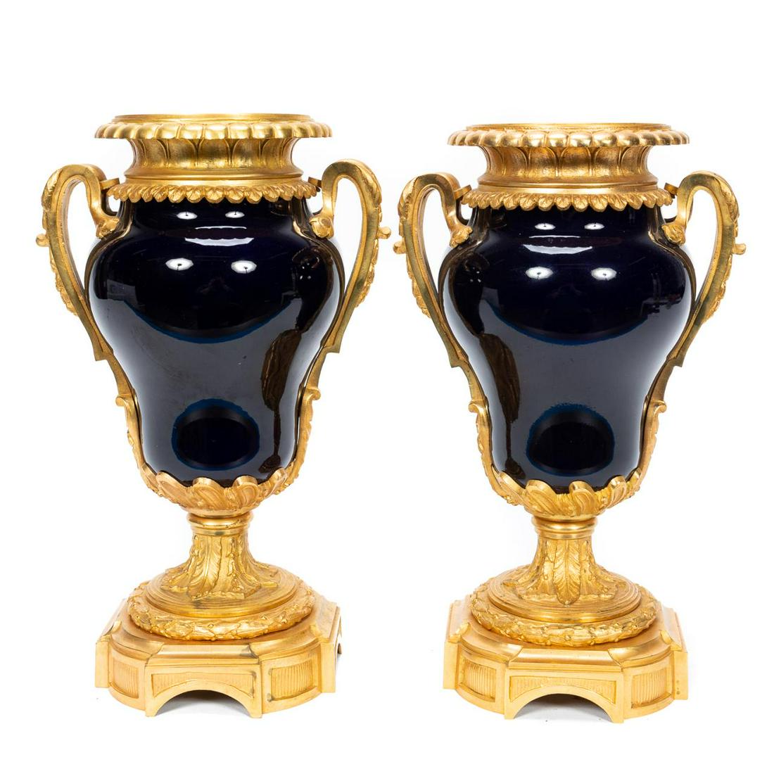 Pair, Louis XVI Style Gilt Bronze Mounted Urns: Possibly Continental, 20th century. Pair of Sevres style, cobalt blue porcelain urns in the Louis XVI taste having foliate gilt bronze ormolu mounts. Unmarked. Approx. of one, h. 13.5", base 5.75" sq.