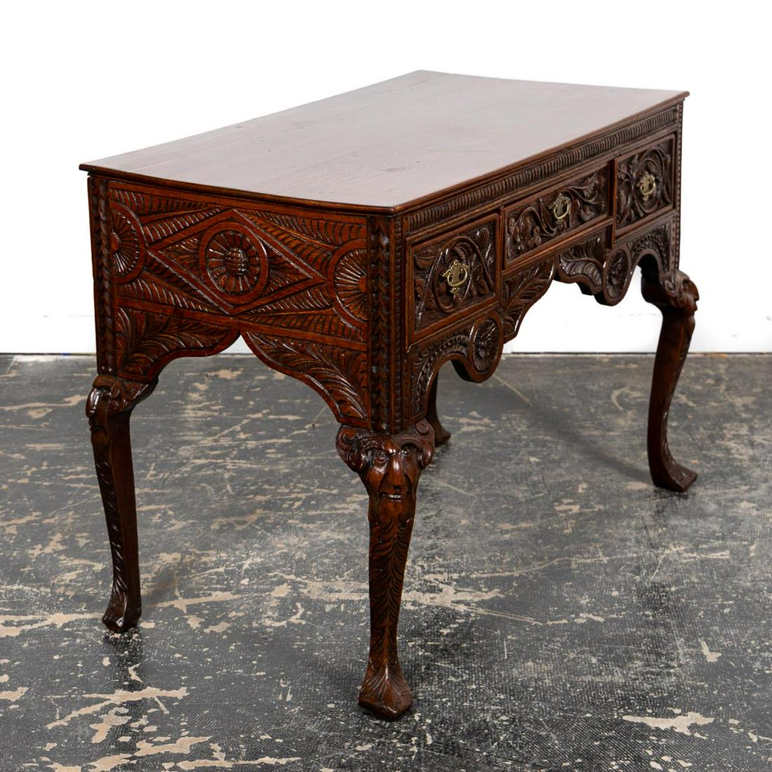 19th C. Carved Oak Antiquarian Dressing Table: English, 19th century. Elaborately carved Victorian era oak dressing table or small desk in the antiquarian gothic taste having three drawers, foliate detail and rising on cabriole legs with figural m