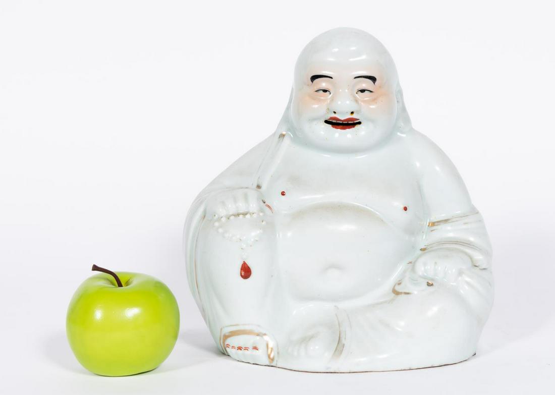 CHINESE WHITE PORCELAIN HOTAI FIGURE, SEATED: Chinese, late 19th century. Porcelain figure of Hota, depicting the fat, cheerful, seated Buddha with hand-painted face, prayer beads in one hand and holding his robe in the other, iron red and gold p