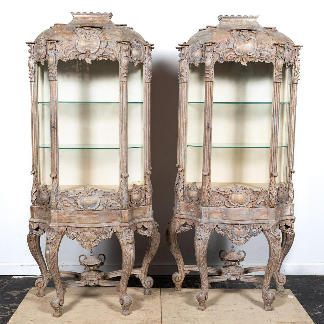 PAIR, 20TH C. REGENCE STYLE VITRINE CABINETS: French, early 20th century. Pair of wooden vitrine cabinets on stands in the Regence rococo taste having a limed finish, domed tops, the friezes and cases decorated with foliate cartouches, each with 