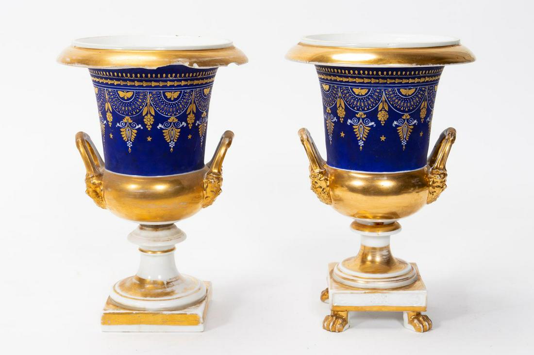 NEAR PAIR OLD PARIS MATTE DECORATED PORCELAIN URNS: French, 19th century. A near pair of old Paris porcelain urns with a matte blue decorated body accented by gilt foliate and butterfly decorations, grotesque mask figural handles and one resting on fou