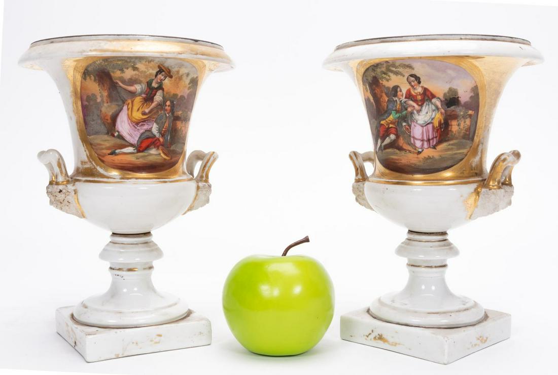 PAIR, 19TH C. OLD PARIS URNS WITH FIGURAL SCENES: 19th Century, French, Pair of Old Paris Porcelain Urns. Campana shape with mascaron handle terminals, decorated with panels of courting couples and floral sprays. Approx. 9.125" H, 6.5" Dia. Provenanc