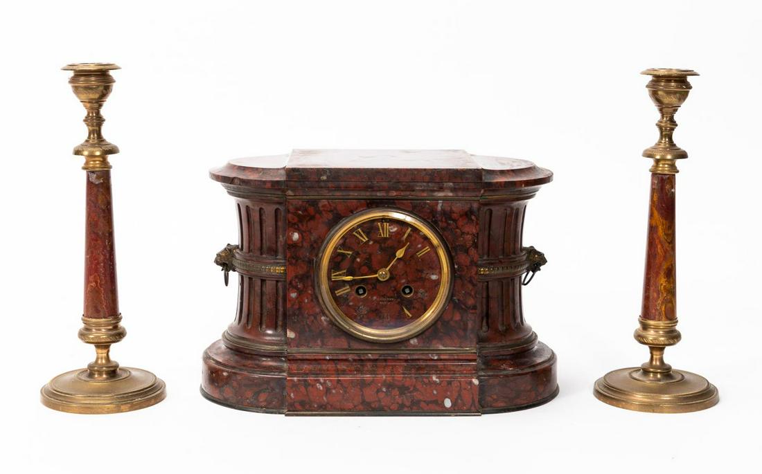 FRENCH BARBEDIENNE MARBLE & BRONZE GARNITURE SET: Barbedienne Foundry (French, 1838-1952), late 19th century. A three-piece rouge red marble and bronze garniture set having an eight day movement mantle clock, roman numeral dial with fluted pillar sid