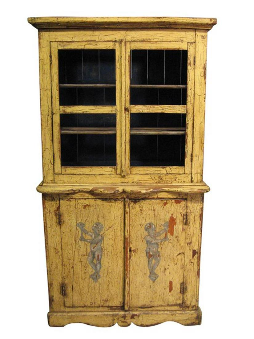 SMALL PAINTED CUPBOARD IN YELLOW, CIRCA 1890-1920: Continental, 1890-1920. Distressed yellow painted pine cupboard having a shaped cornice above double doors, serpentine lip above double doors decorated with cherubs, on a scalloped plinth. Unmarked. A