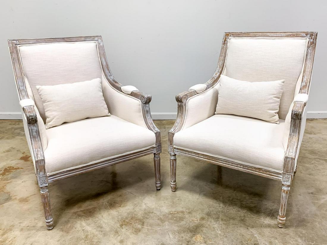 PAIR, DISTRESSED LOUIS XVI STYLE BERGERE CHAIRS: Pair of contemporary enclosed armchairs in the Louis XVI taste having a linen-like upholstery, white painted distressed frames and rising on tapered fluted legs. Manufacturer's label to the underside.